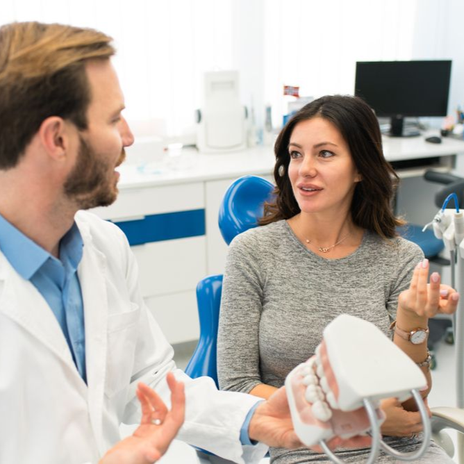 Dentist showing a patient a model of teeth in a dental office.
