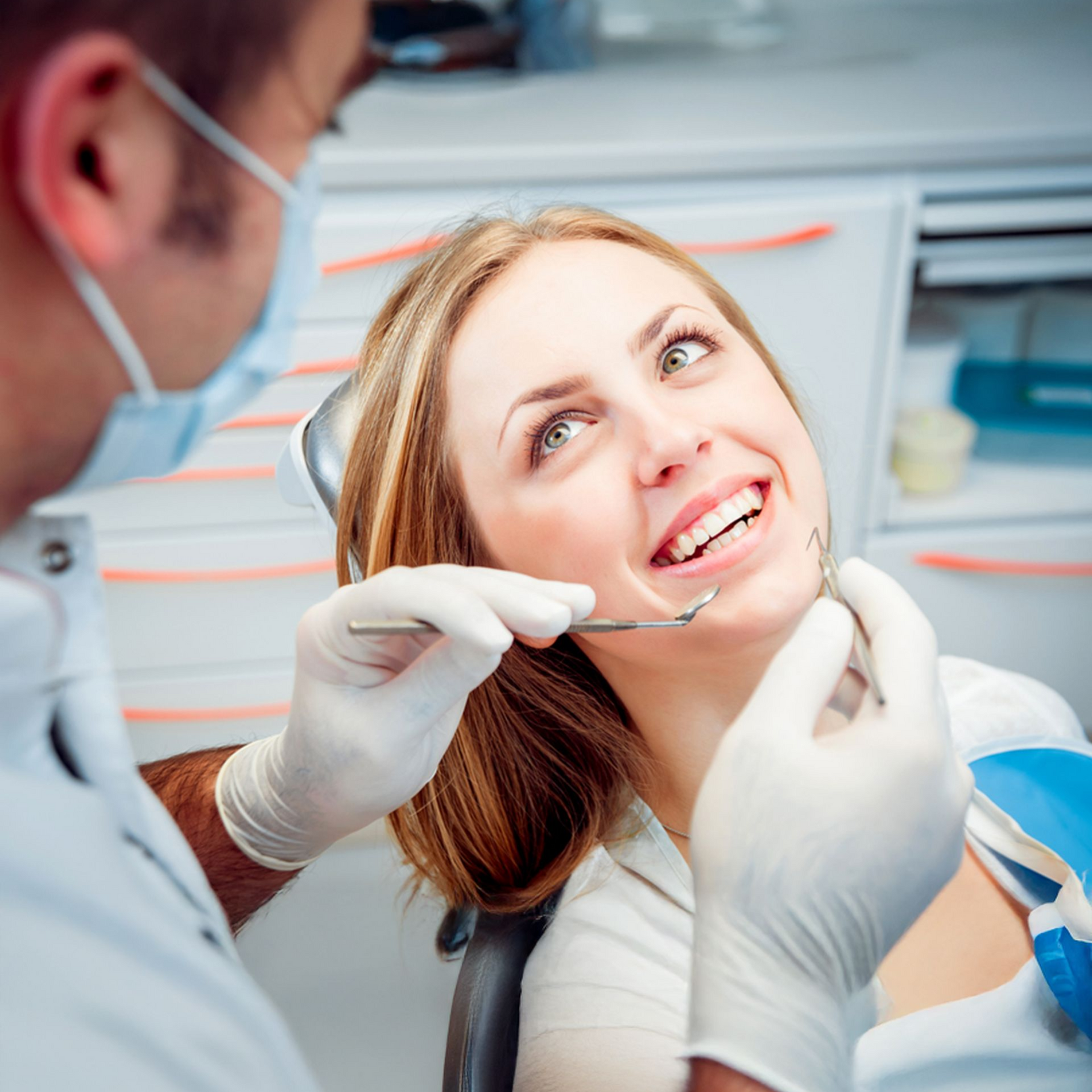 Dentist examining a patient's teeth. The patient smiles, looking up. The setting is a dental office.