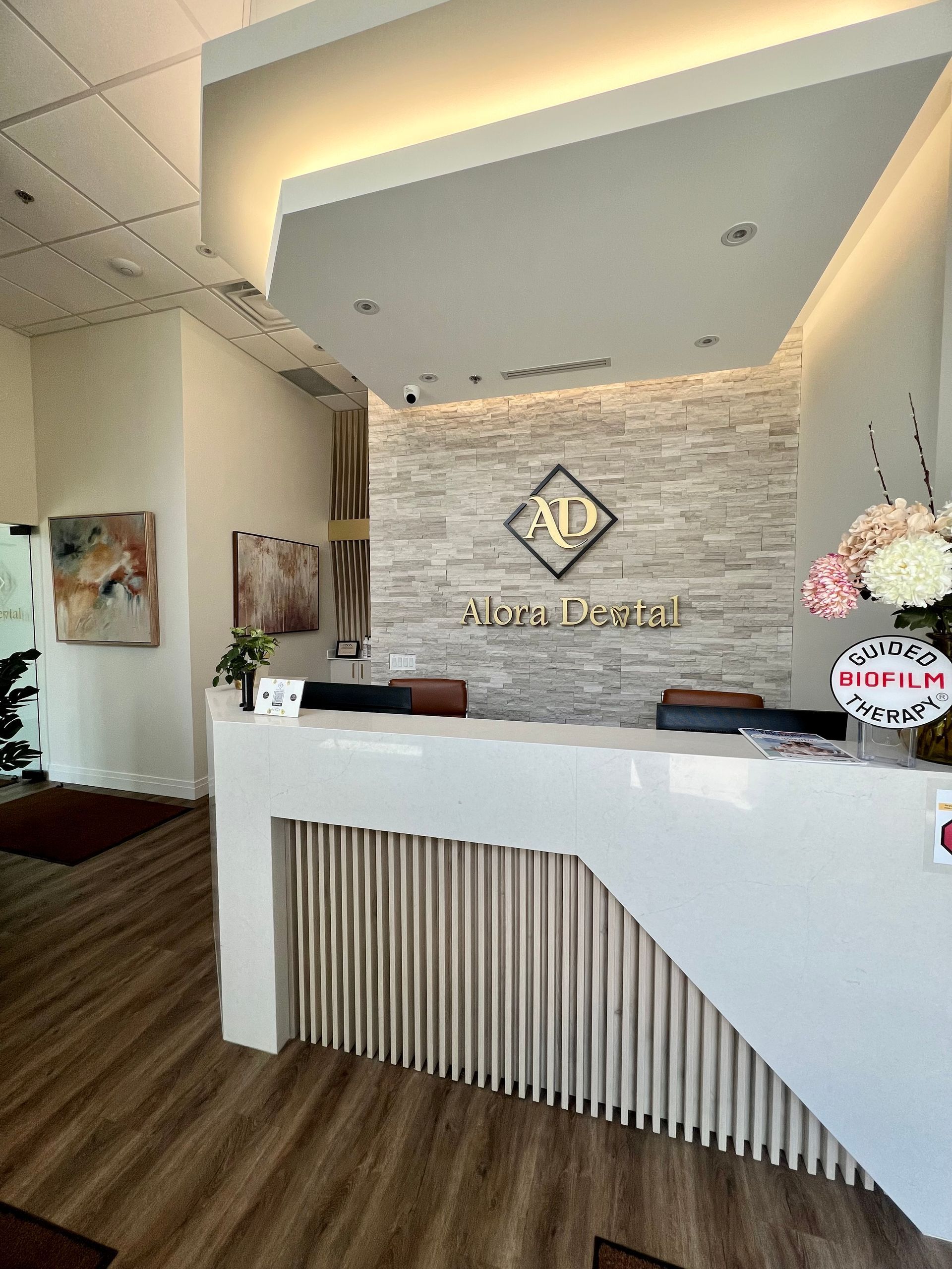 Reception desk with a light-colored wood floor, white counter, and stone accent wall with logo.