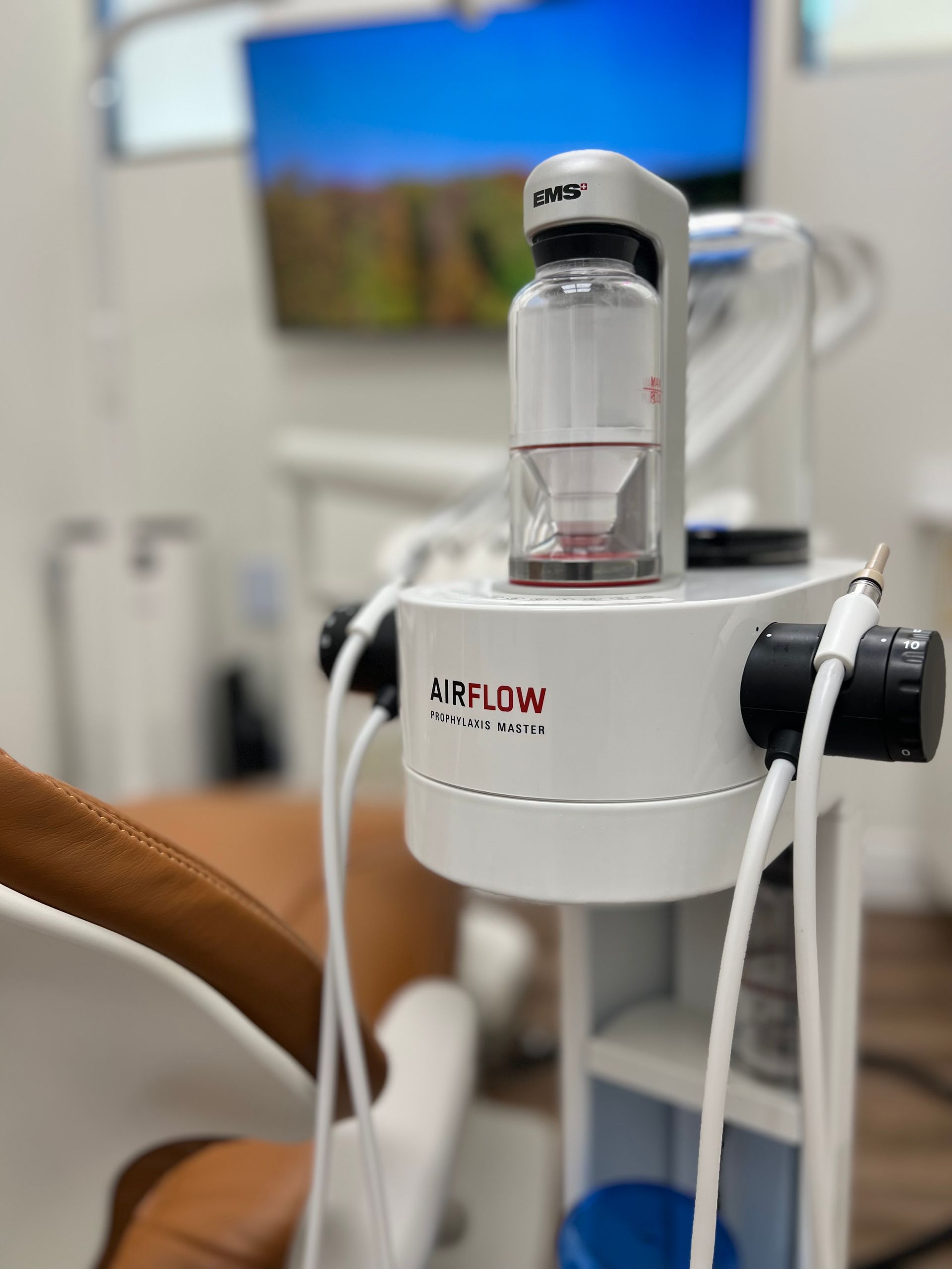 Dental office equipment, including an AIRFLOW unit, in a medical setting, with a dental chair in the foreground.
