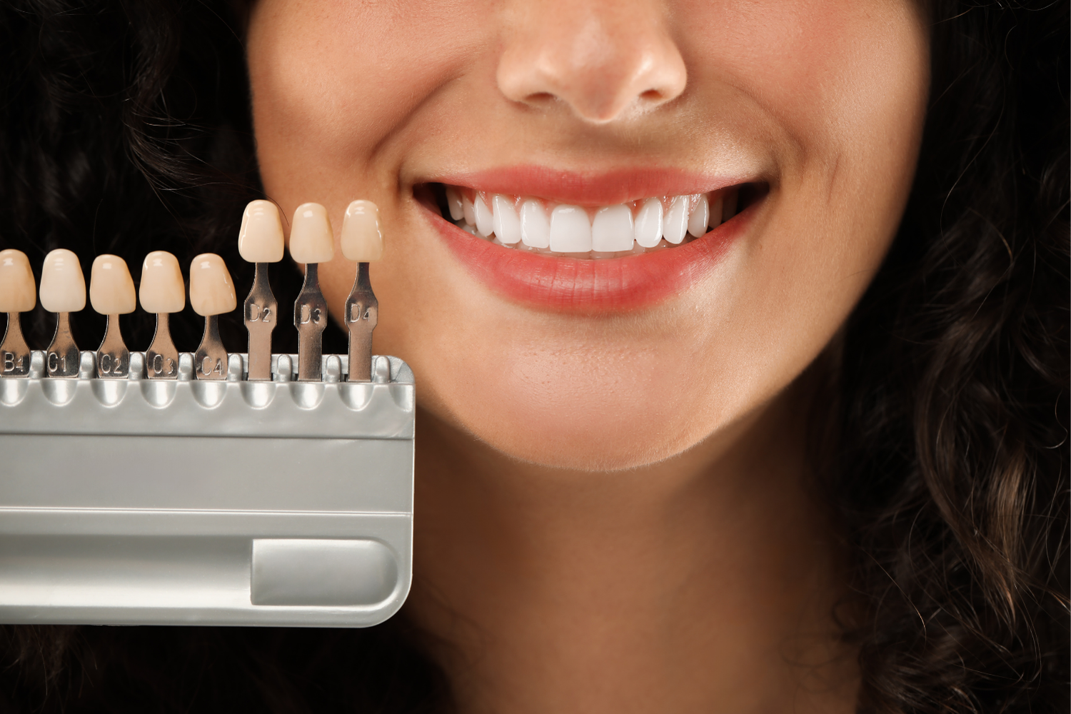 Smiling woman with bright white teeth beside a dental shade guide.