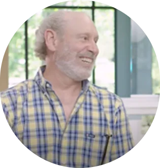 Smiling man in a yellow plaid shirt indoors near a window