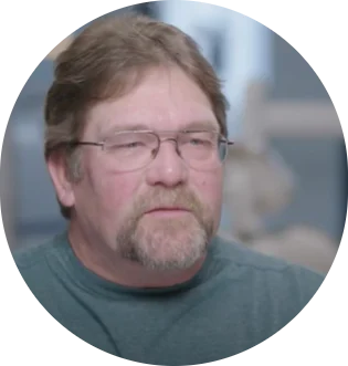 Portrait of a man with glasses and a goatee, wearing a teal shirt, against a blurred background
