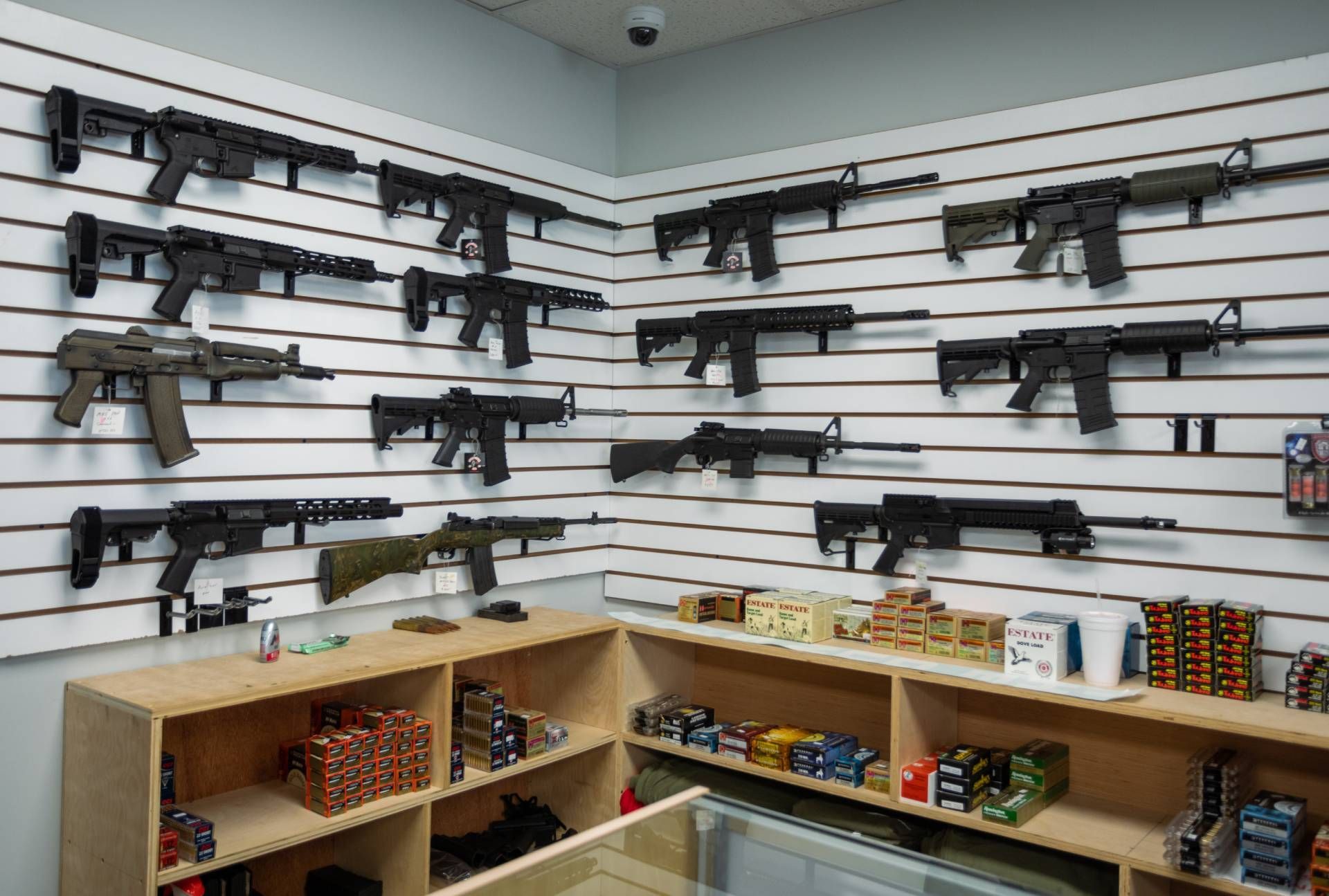 A gun store interior displaying various rifles on the wall, with ammunition and accessories on shelves below.