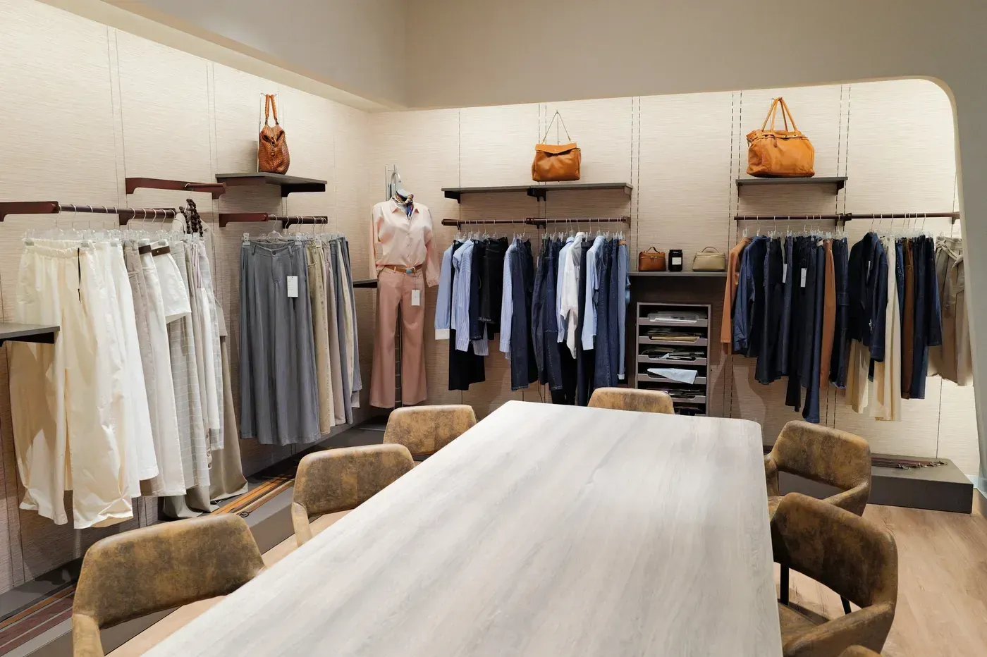 Boutique di abbigliamento con scaffali pieni di capi dai toni neutri e un lungo tavolo al centro.