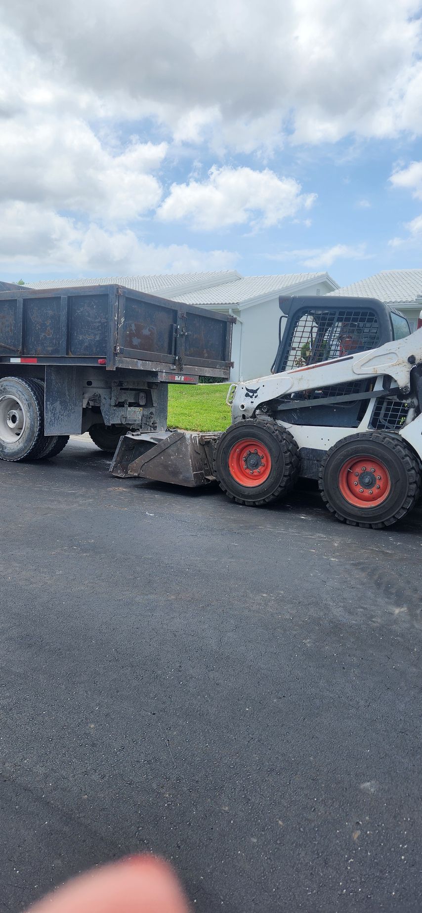 A blue dump truck is driving down a road with trees in the background.