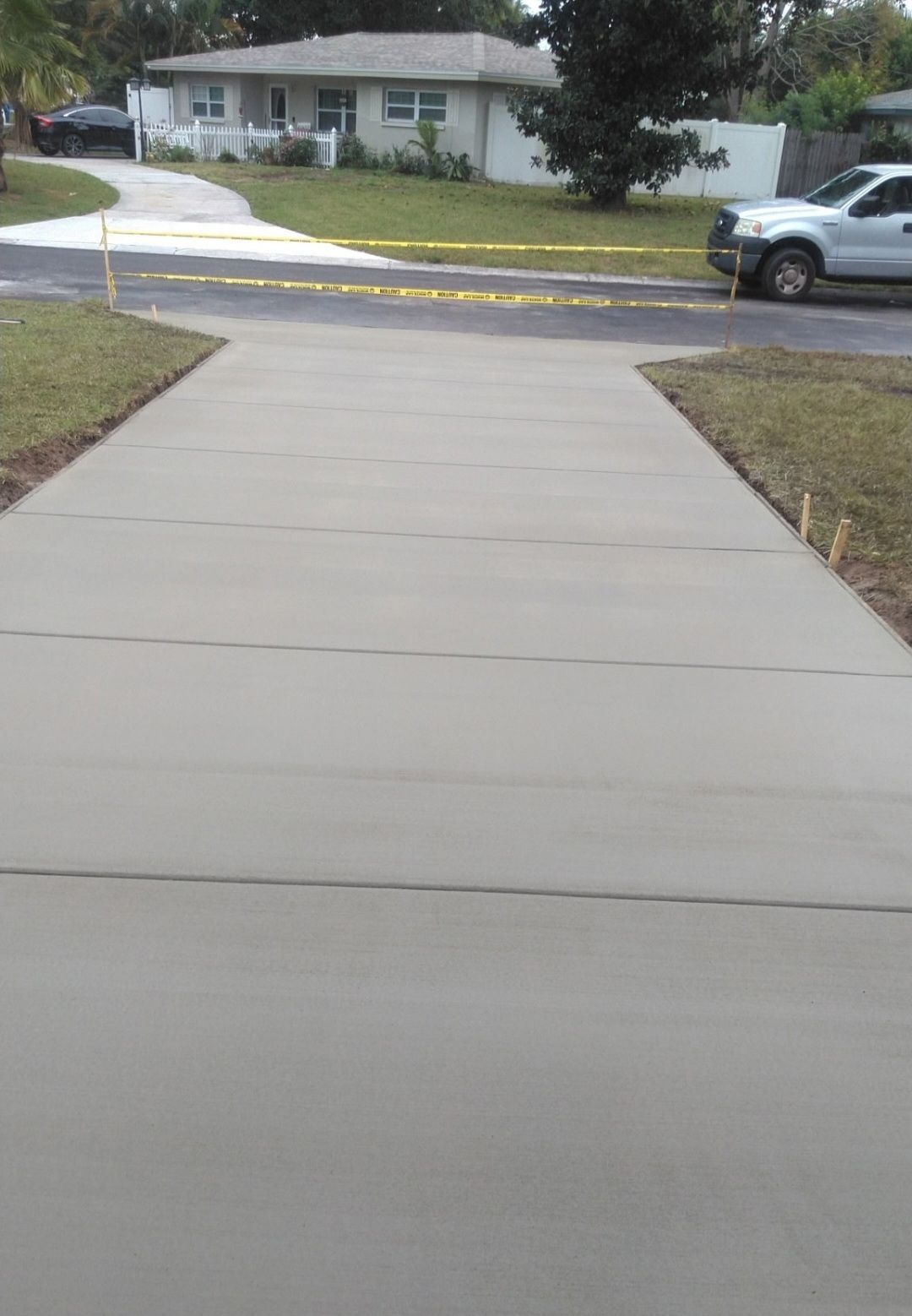 A white truck is parked on the side of a concrete driveway next to a house.