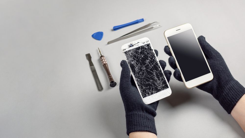 Hands in Black Gloves Holding a Cracked Phone Next to a Working Phone — Micromac Computers in Charmhaven, NSW