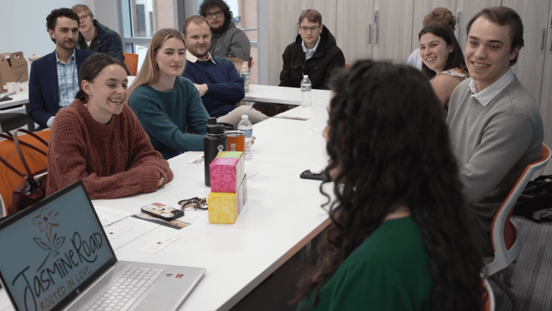 People gathered around a white table in a meeting room, smiling and talking during a group discussion.