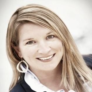 Smiling woman with blonde hair in a white shirt and dark jacket, wearing large hoop earrings