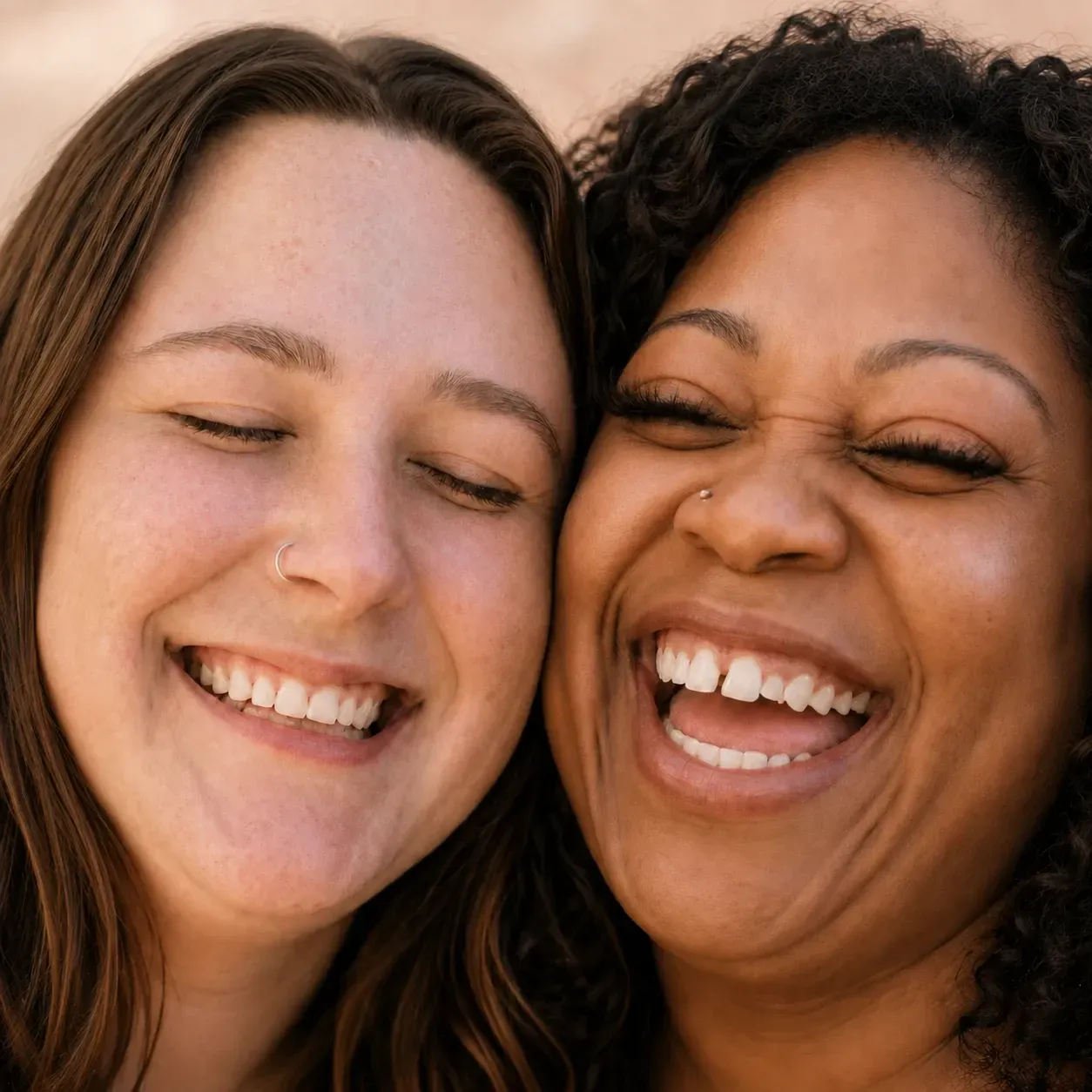 Two smiling faces close together, eyes closed, laughing warmly in soft natural light