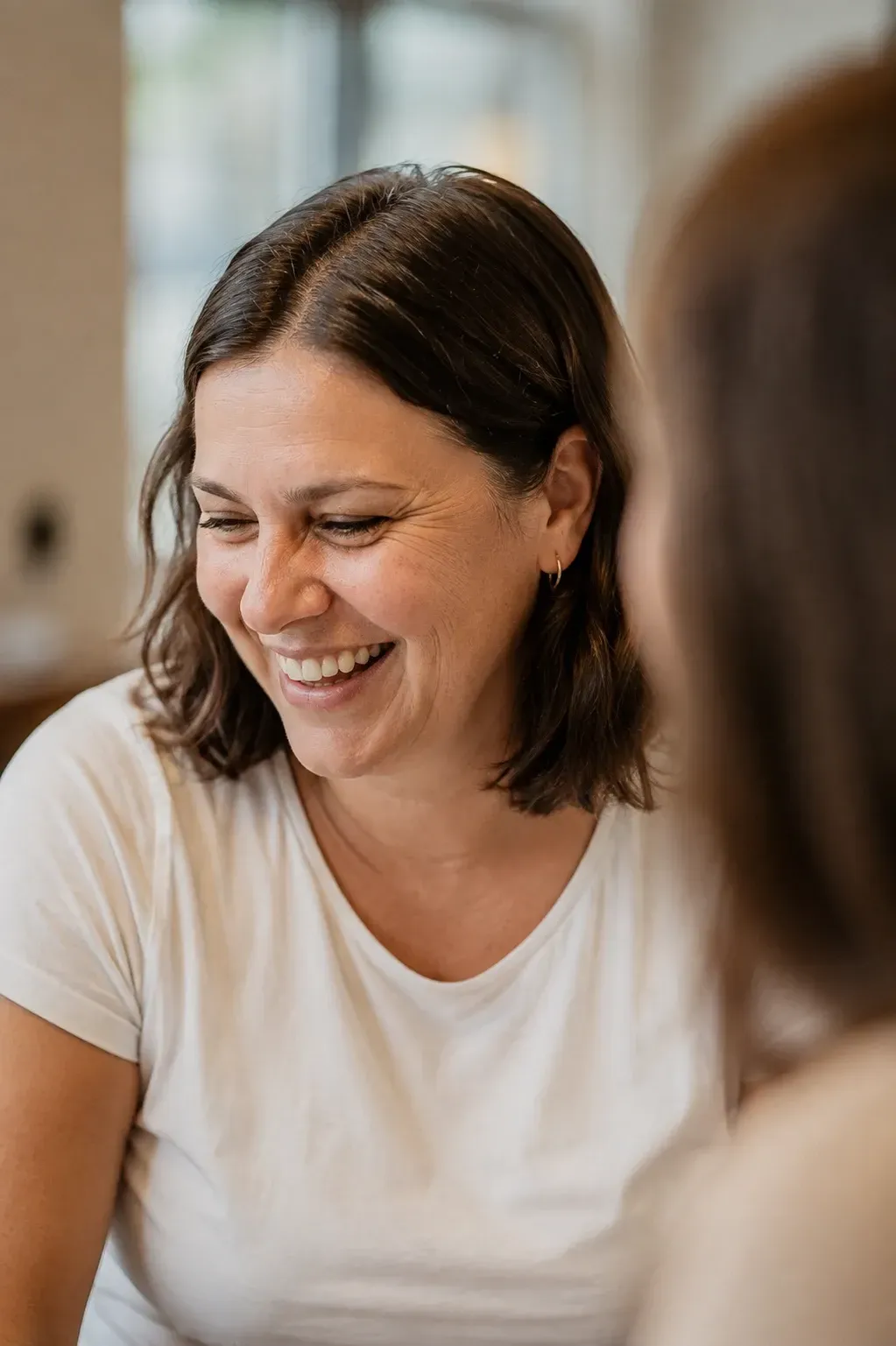 Smiling woman in a white shirt, seated indoors in a softly lit conversation.