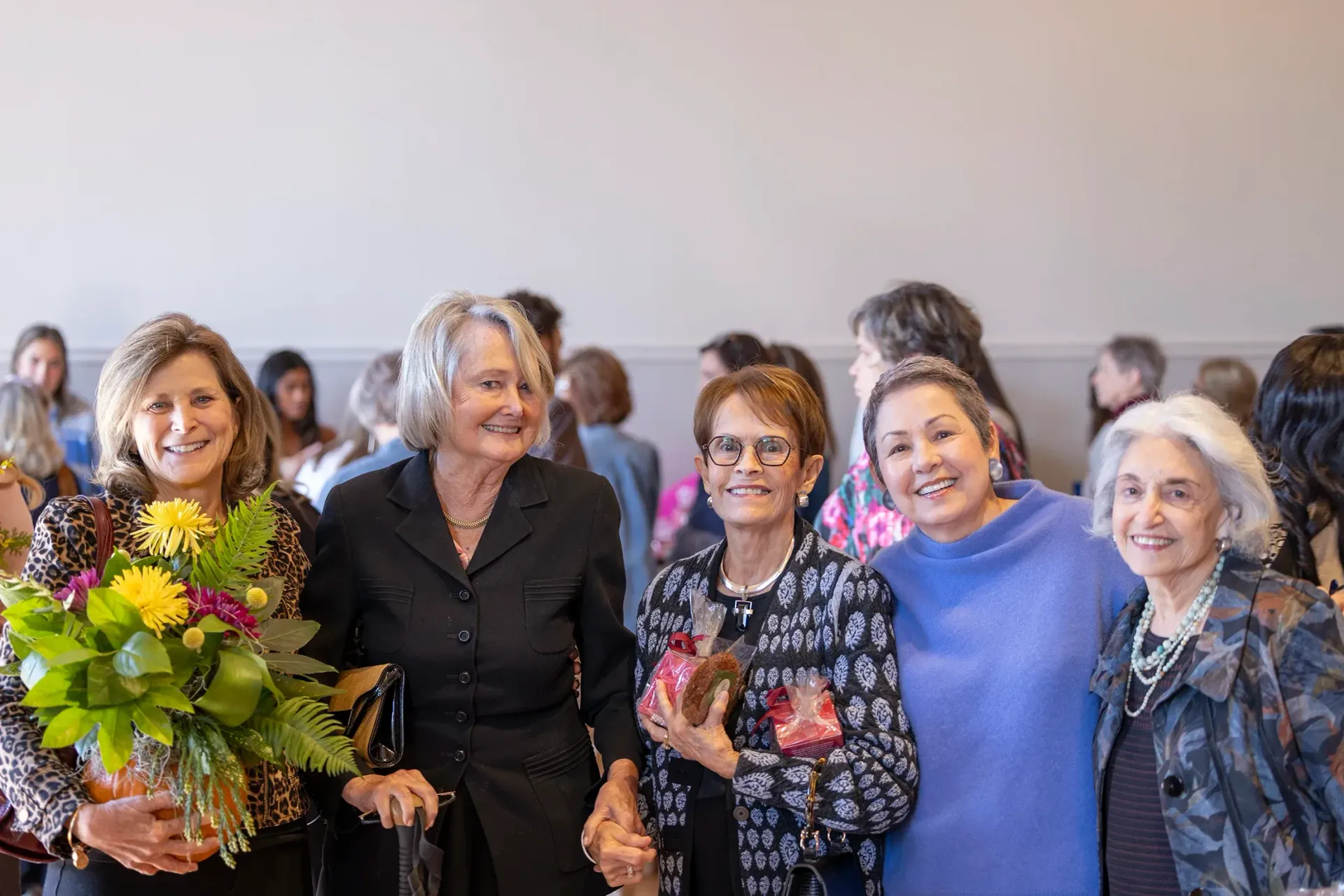 Group of women smiling for a photo, one holding a colorful bouquet indoors