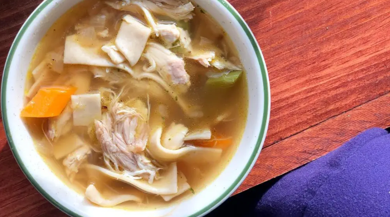 Bowl of noodle soup with chicken and vegetables on a wooden table