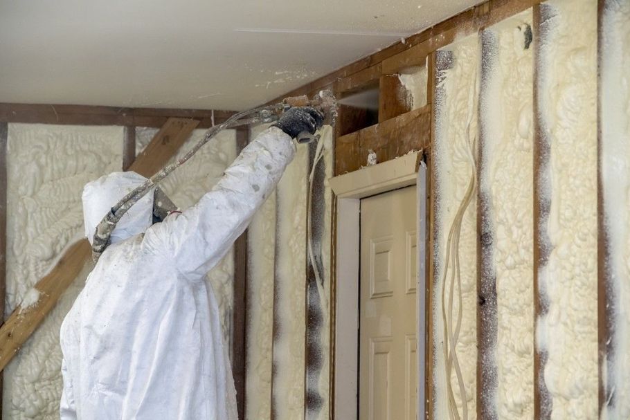 Person spraying insulation into exposed wall studs near a doorway in a room under renovation
