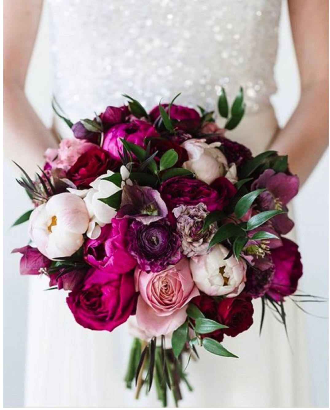 A woman in a white dress is holding a bouquet of purple and pink flowers.