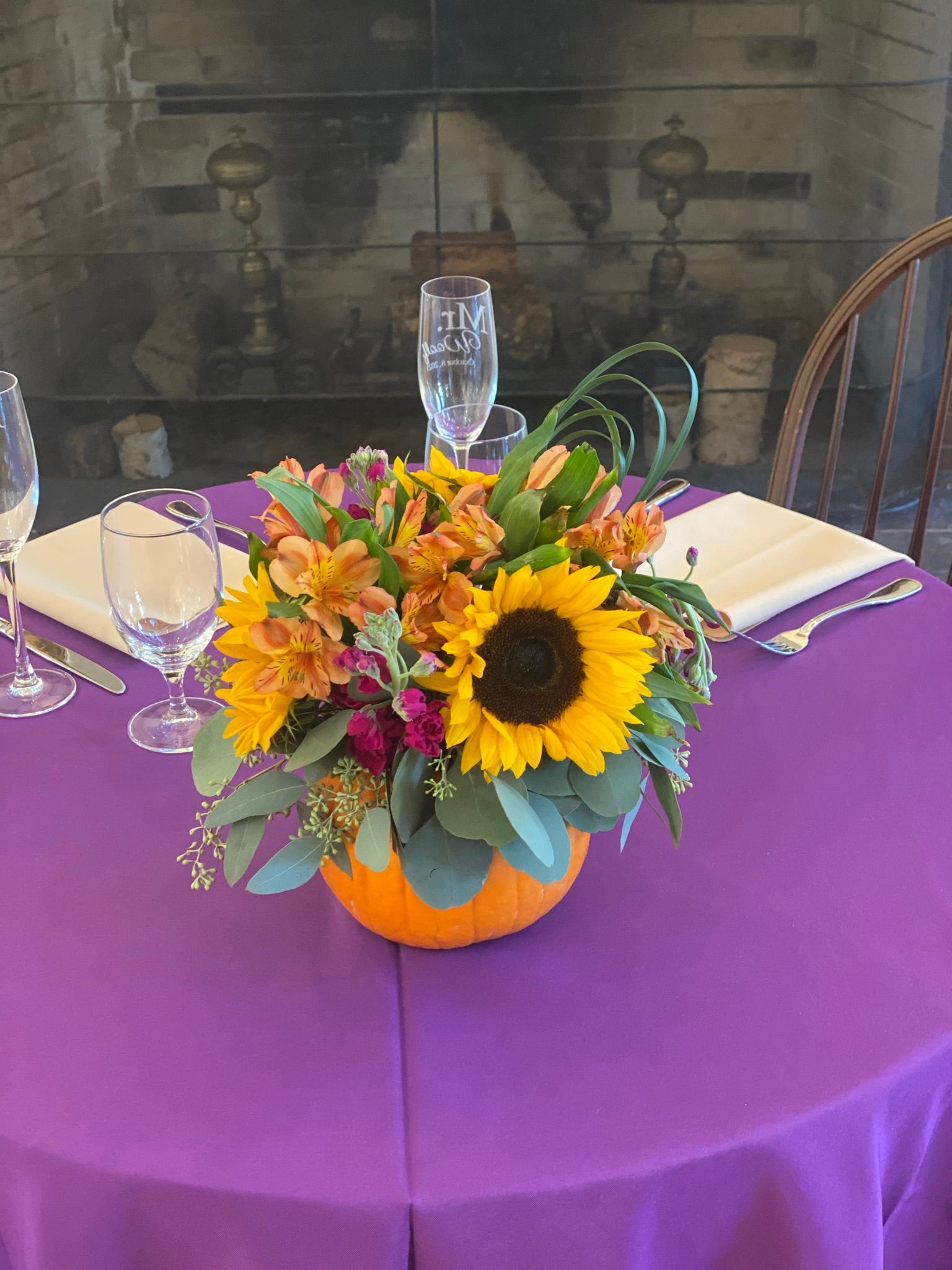 A pumpkin filled with flowers is sitting on a purple table.