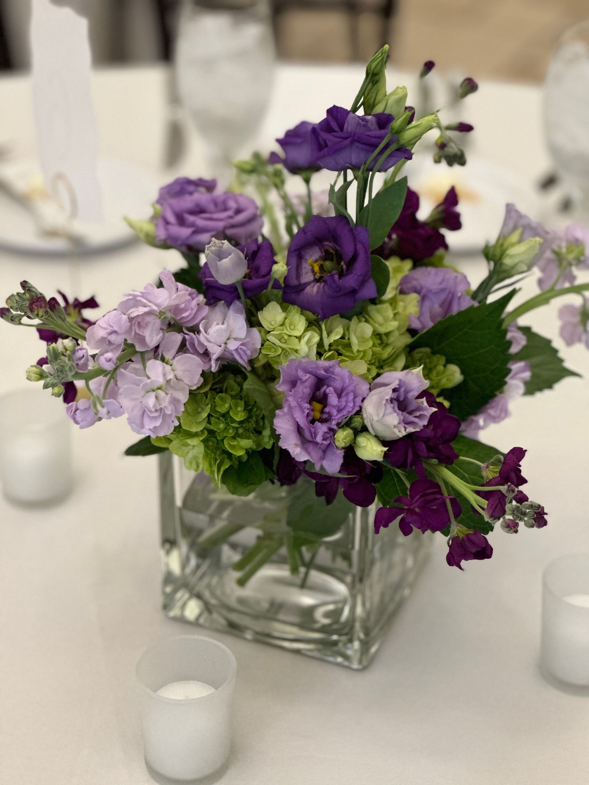 A vase filled with purple flowers and candles on a table.