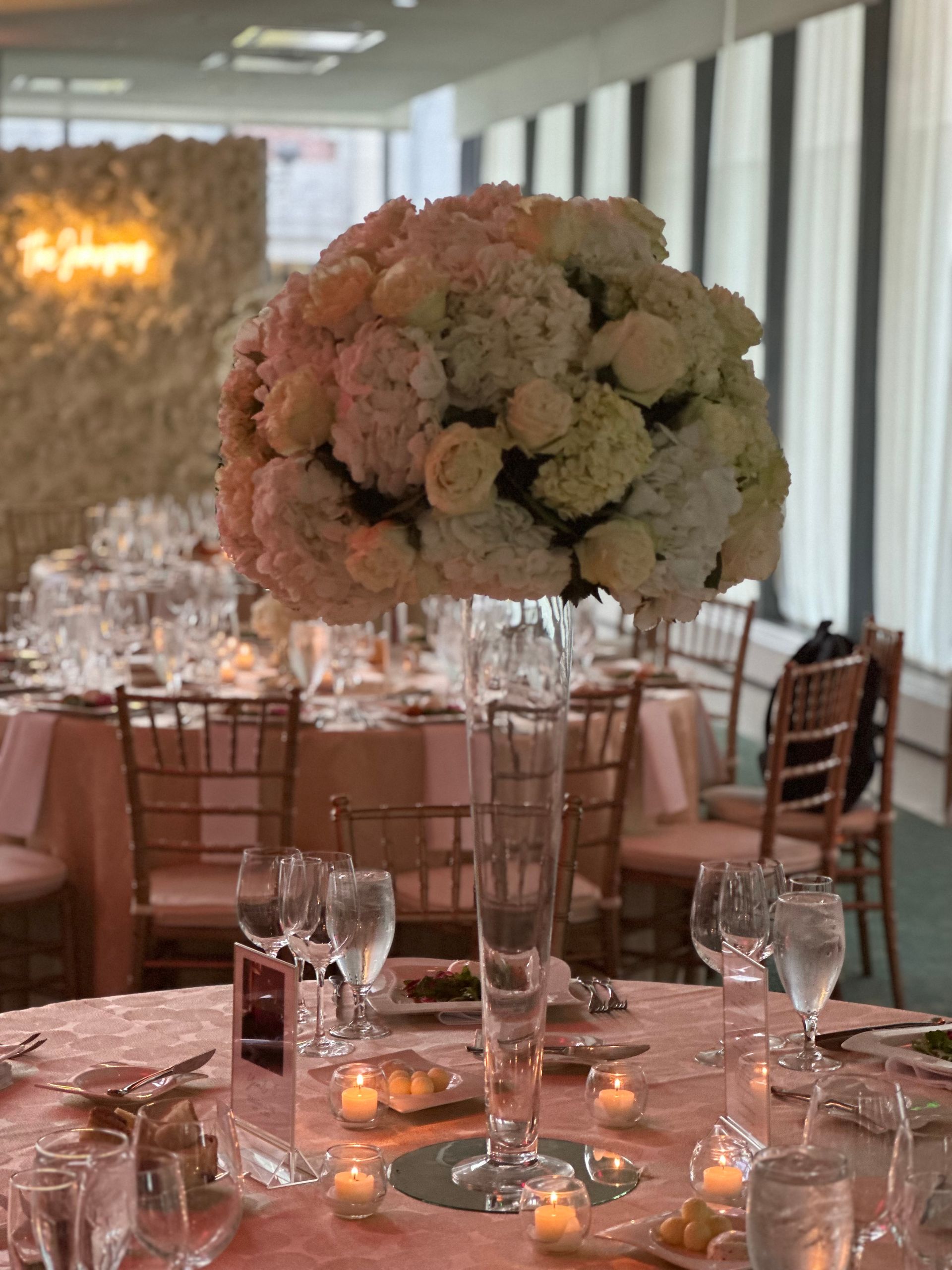 A table set for a wedding reception with a large vase of flowers on it.