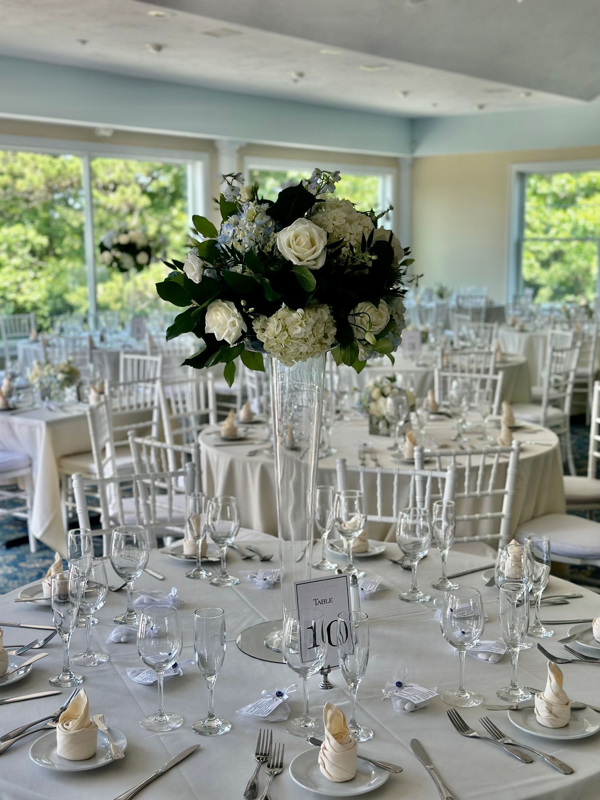 A table set for a wedding reception with a tall vase of flowers on it.