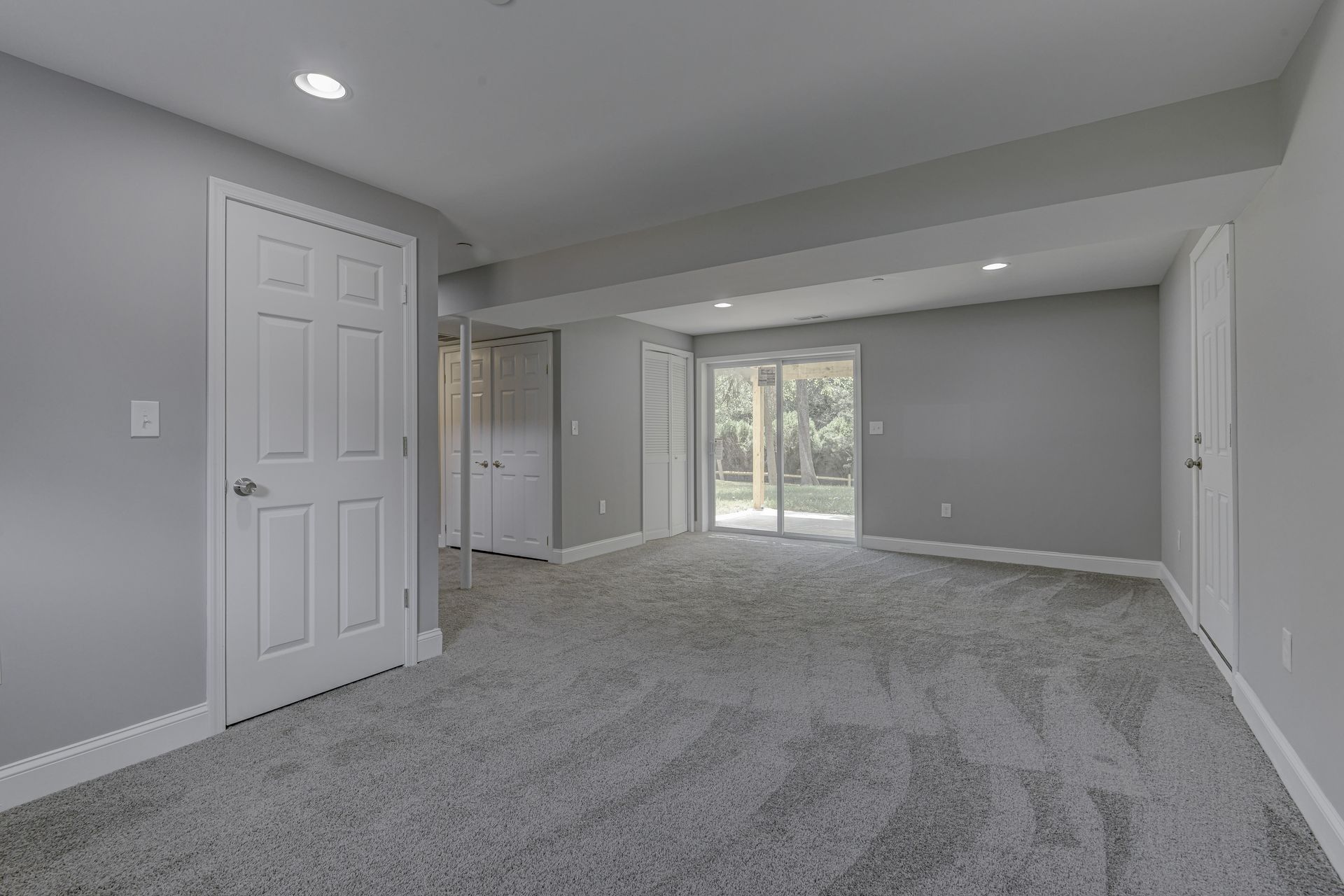 An empty basement with a sliding glass door and gray carpet.