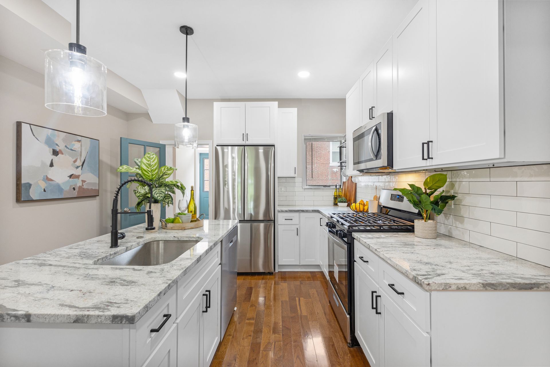 A kitchen with white cabinets , granite counter tops , stainless steel appliances and hardwood floors.