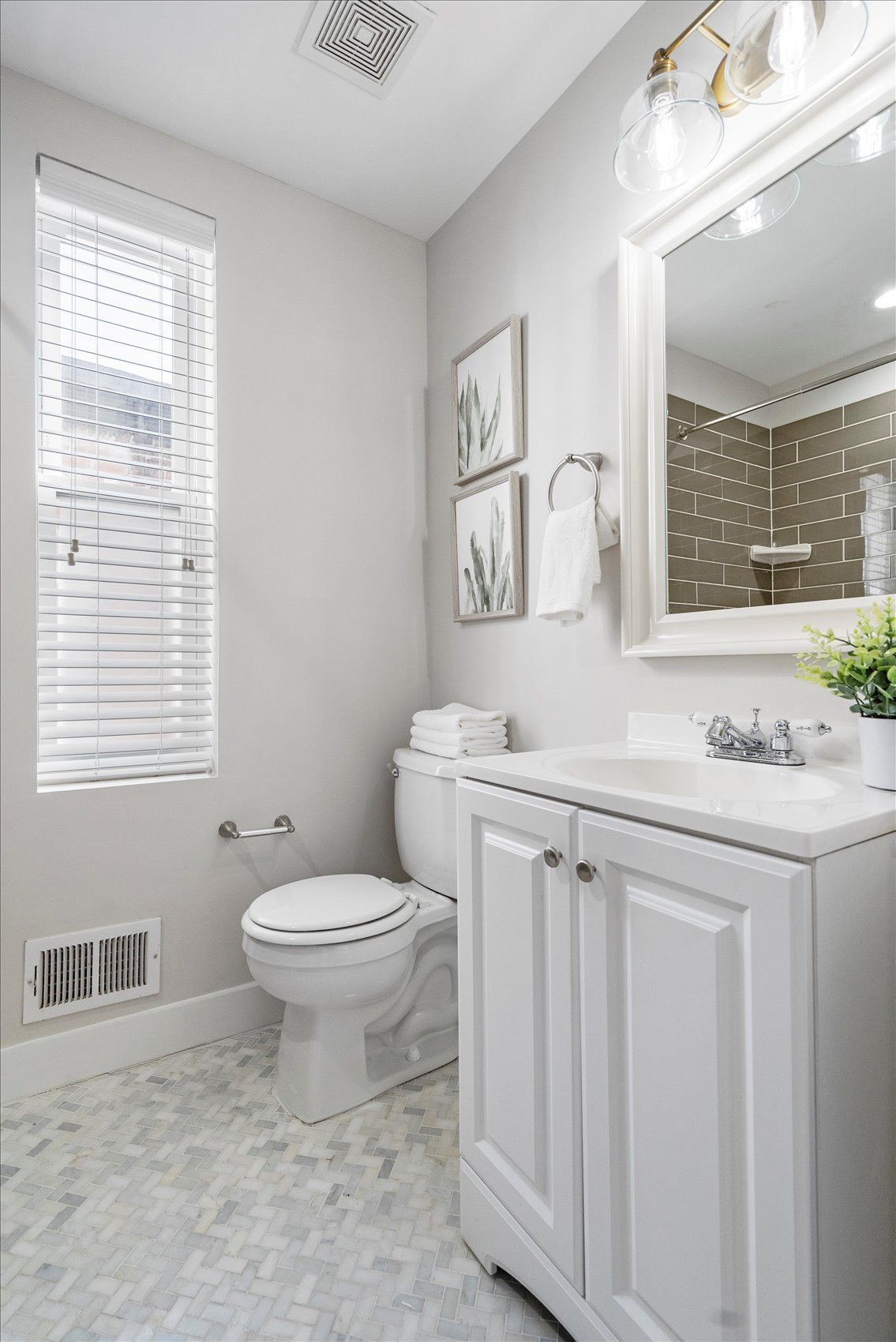 A bathroom with a toilet , sink , mirror and window.
