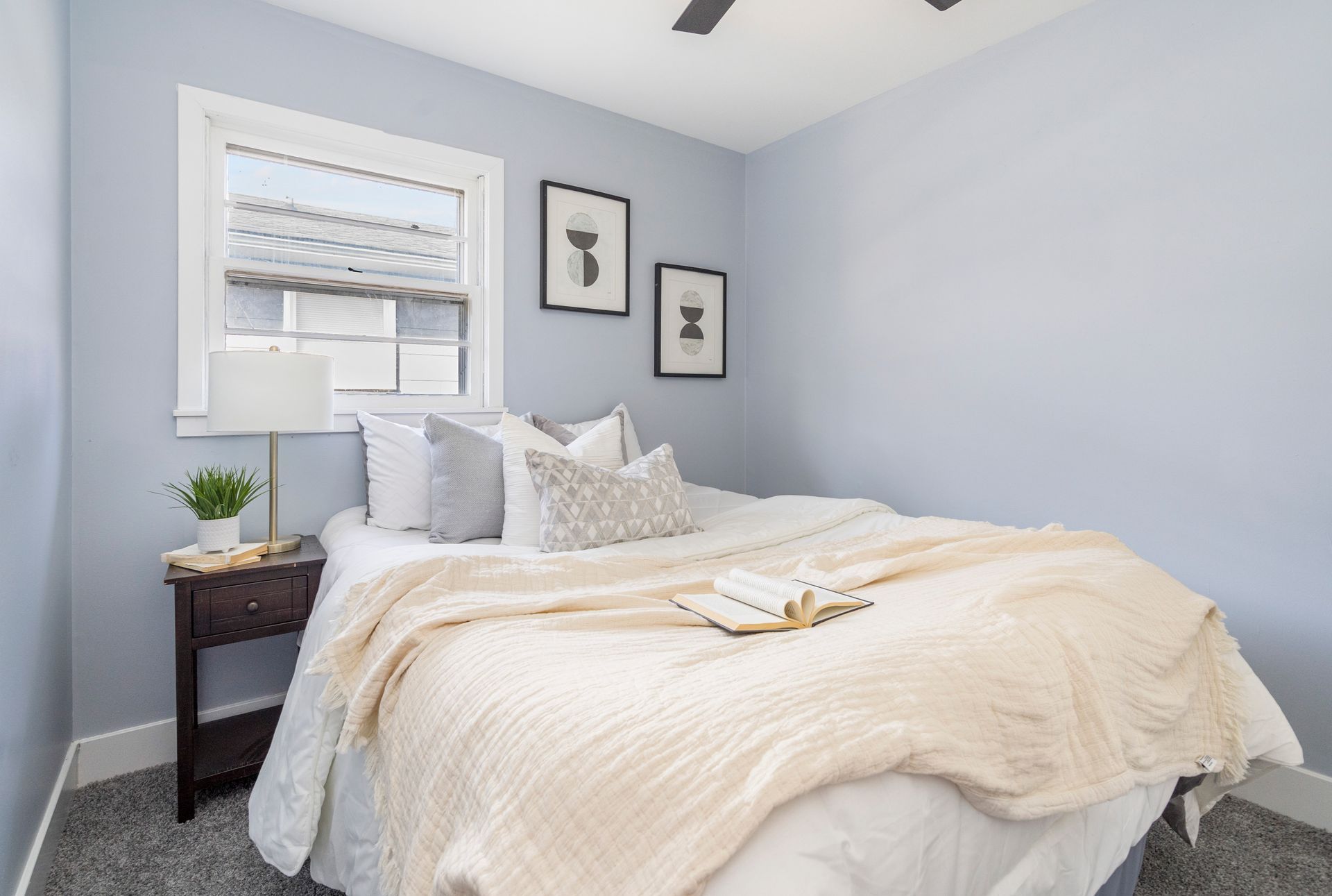 A bedroom with a bed , nightstand , lamp and window.
