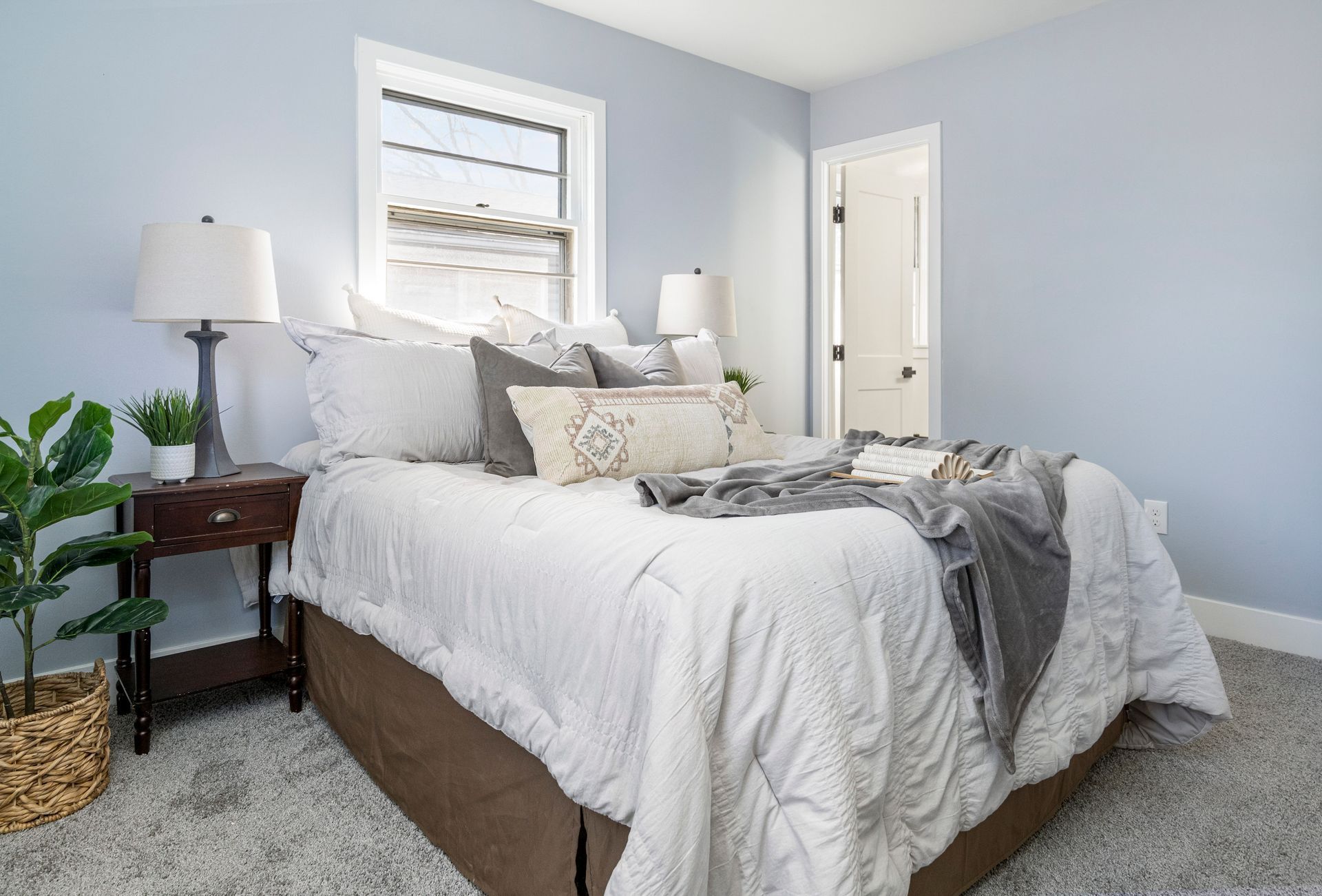 A bedroom with a bed , nightstand , lamp and window.