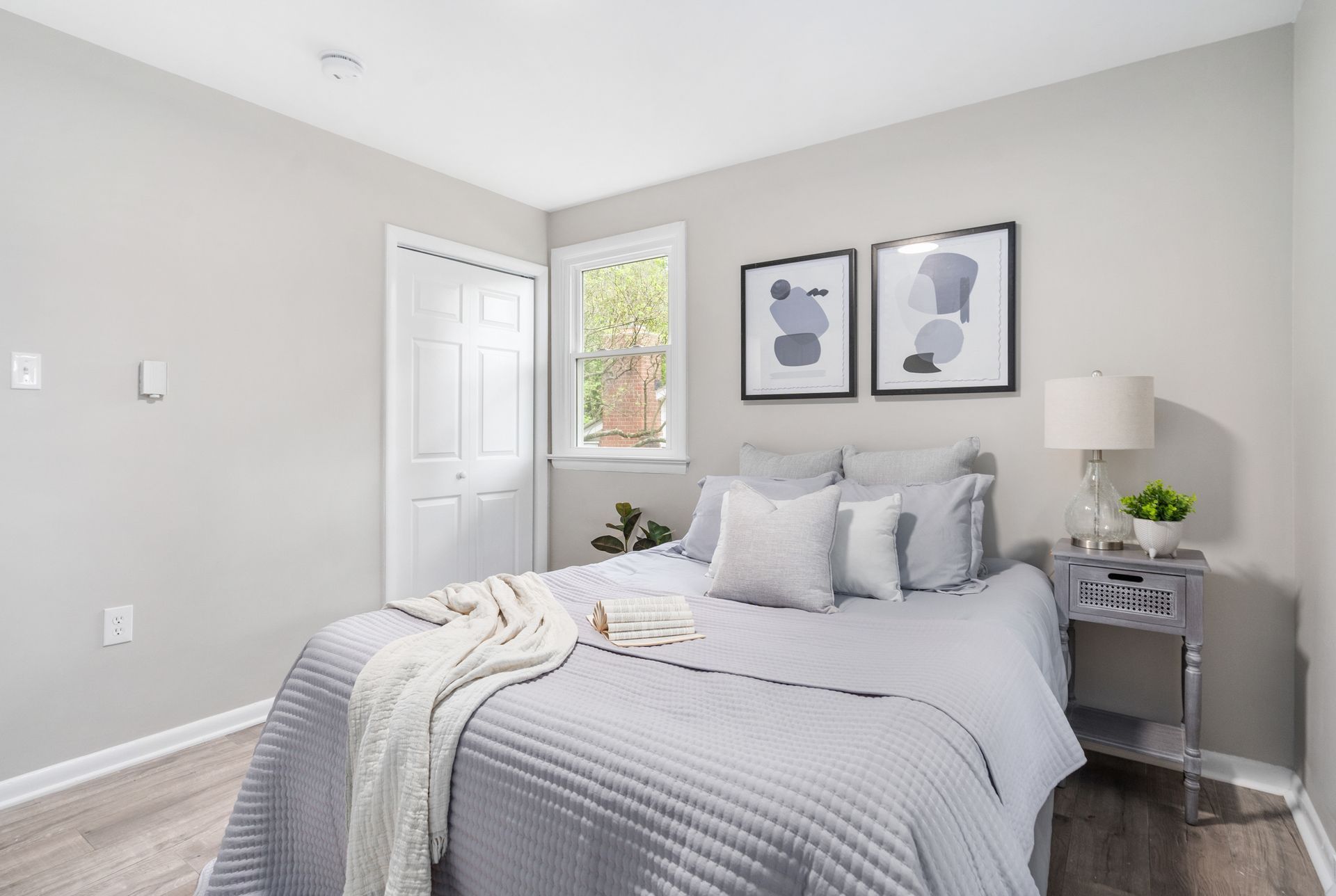 A bedroom with a bed , nightstand , lamp and two paintings on the wall.