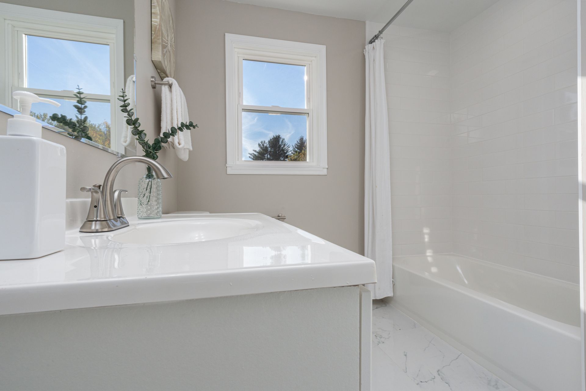 A bathroom with a sink , tub , mirror and window.