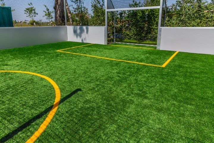 Green turf soccer field with white walls, goal, and yellow lines, outdoors.