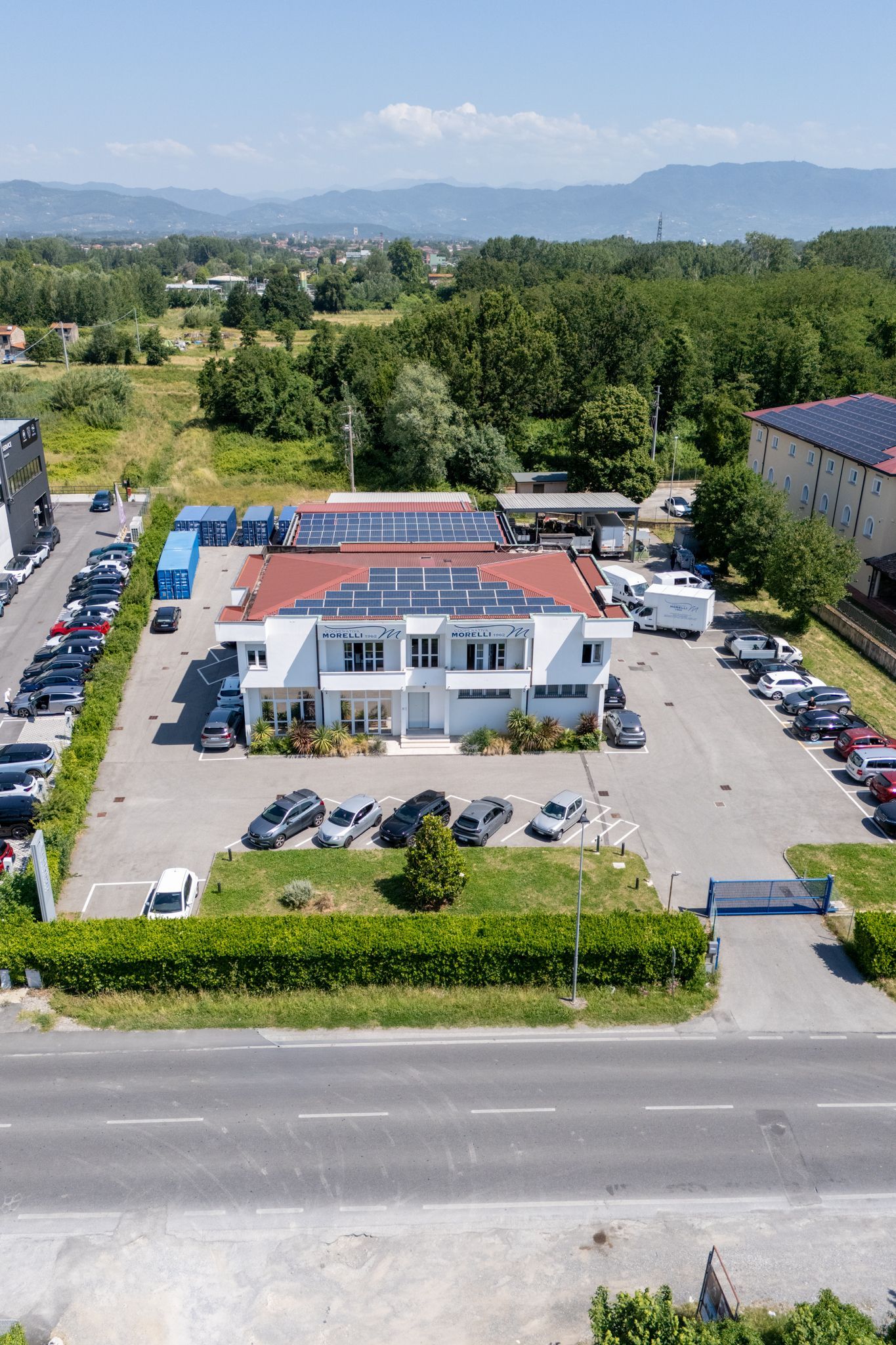 Veduta aerea di un edificio per uffici bianco con tetto rosso, parcheggi e alberi in una giornata di sole.