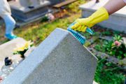 Una mano guantata strofina con una spazzola un monumento di pietra grigia all'aperto.