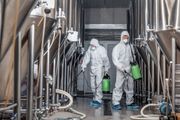 Due operai con tute protettive bianche trasportano contenitori verdi all'interno di un birrificio o di una fabbrica industriale.