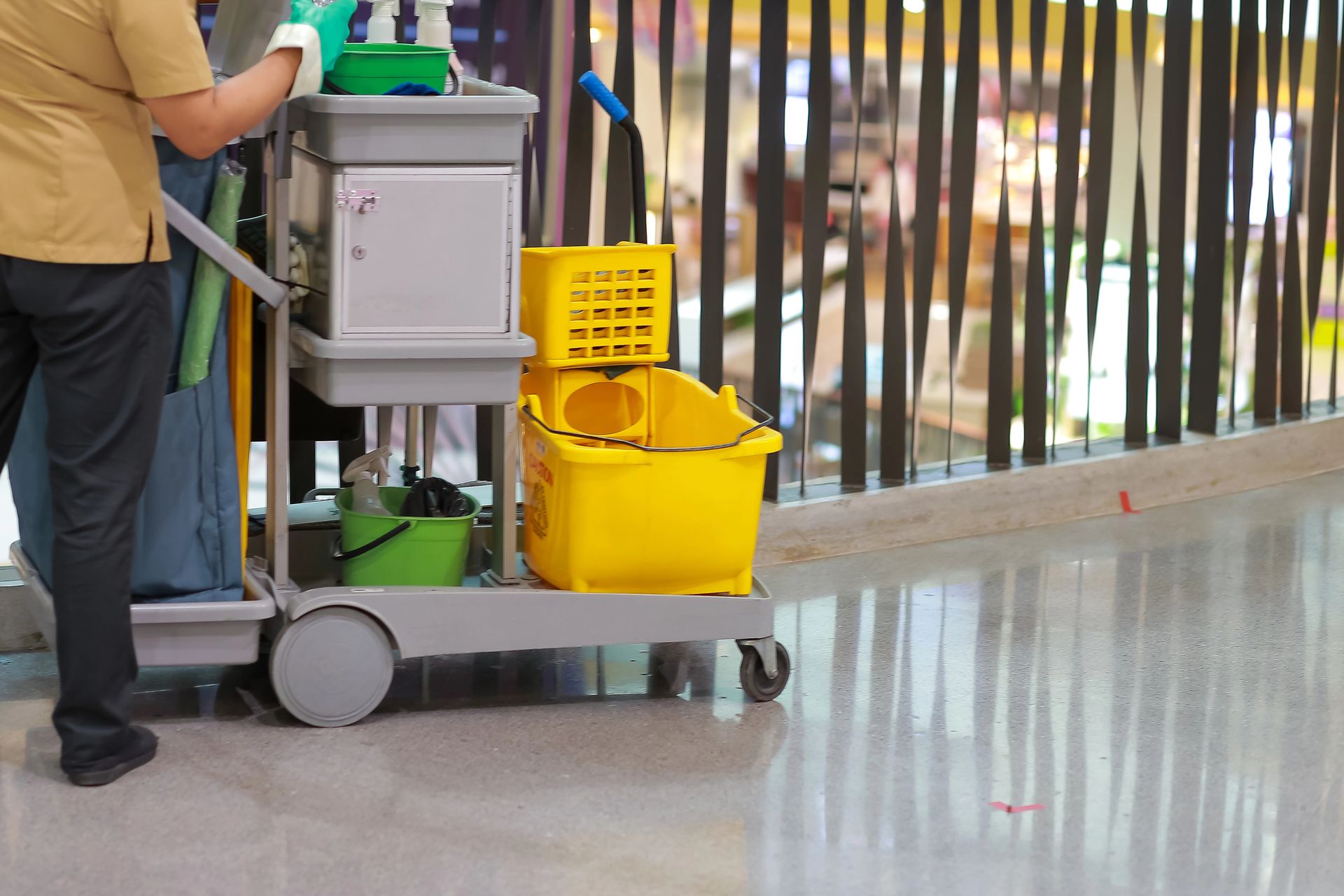 Custodian pushing a cleaning cart with yellow mop bucket in a mall hallway