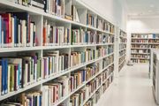 Un corridoio luminoso della biblioteca con scaffali bianchi pieni di libri e un lungo corridoio ben illuminato.