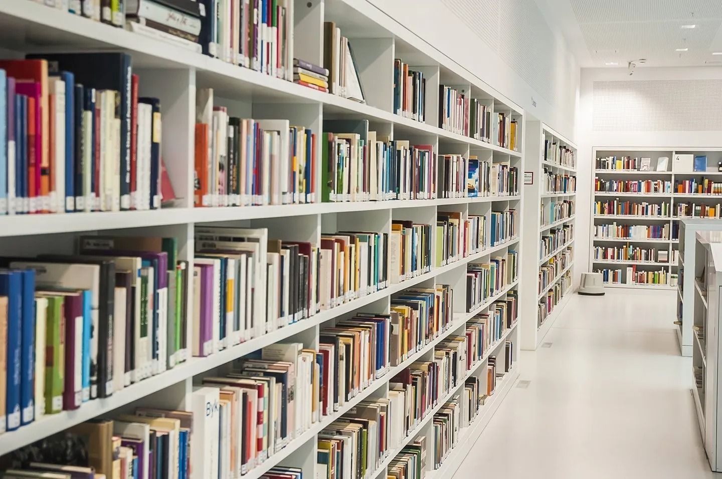 Bright library aisle with white bookshelves filled with colorful books and a long hallway view