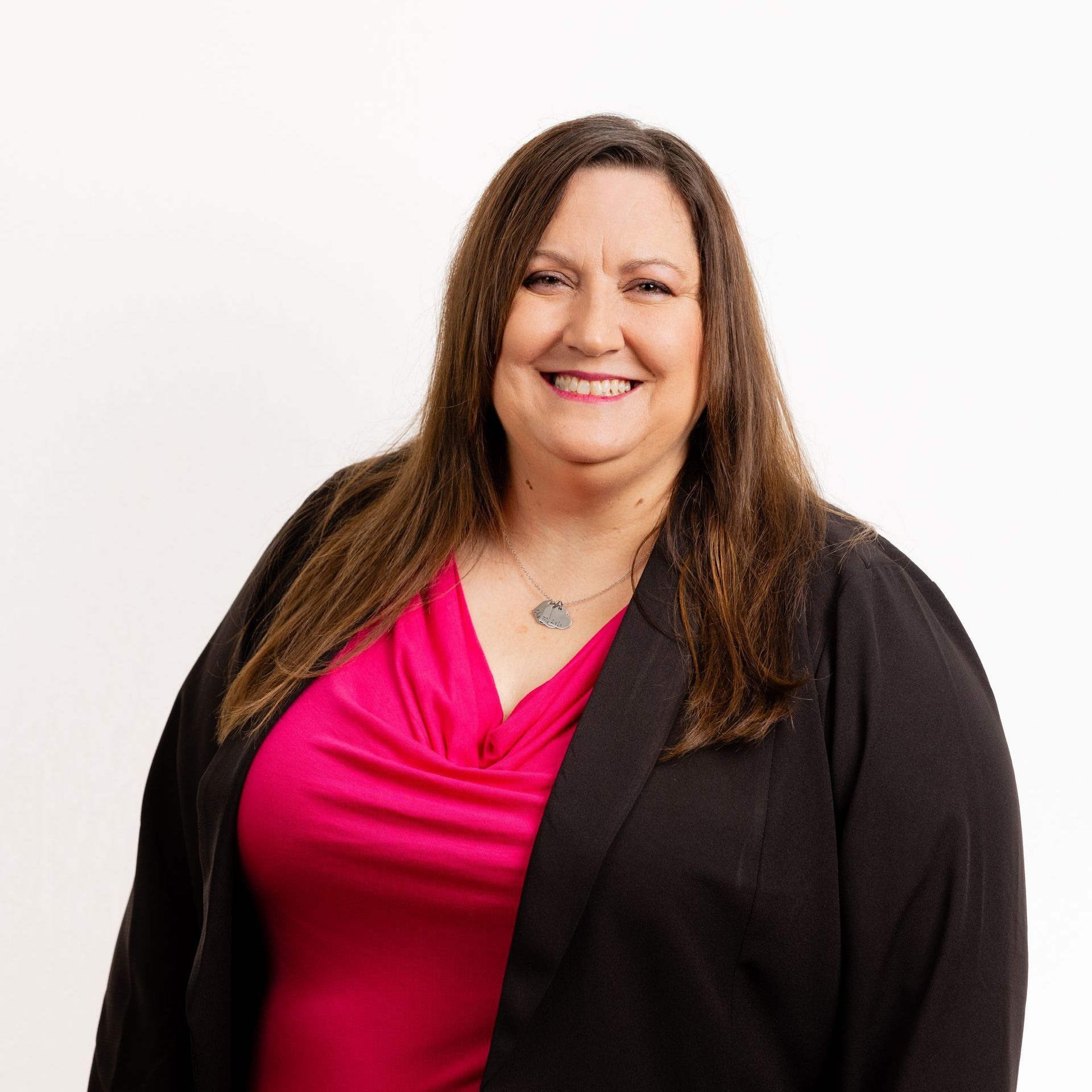 A woman wearing a pink shirt and a black jacket is smiling for the camera.