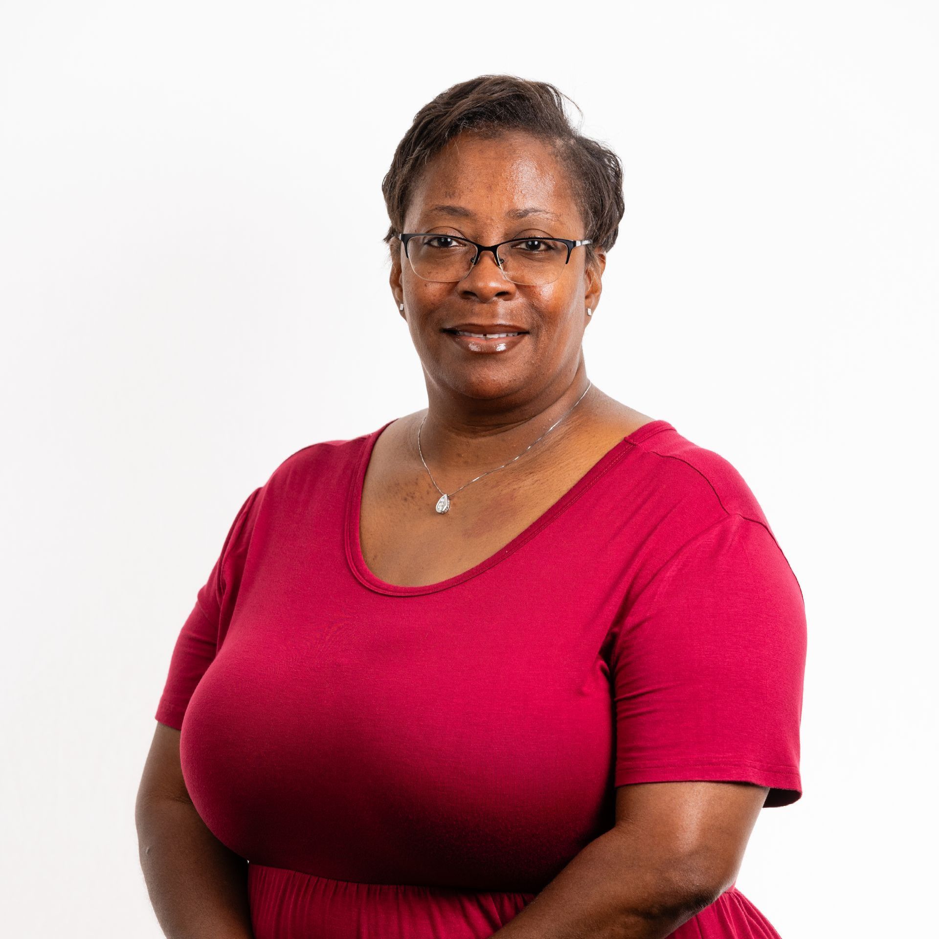A woman wearing glasses and a red shirt is standing in front of a white background.