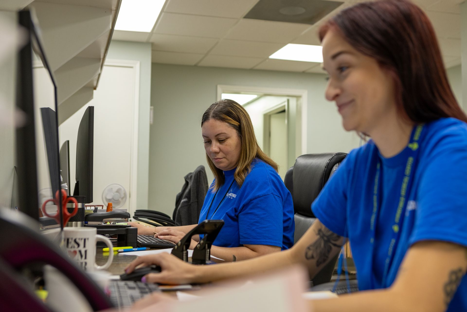 Two women are sitting at a desk in front of a computer.