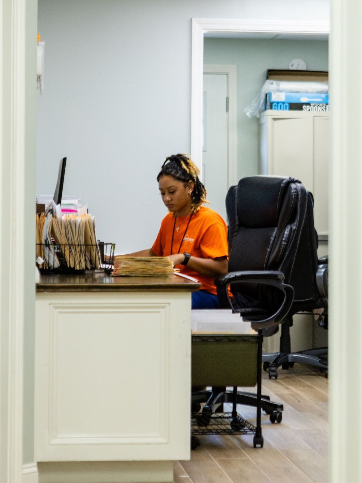 A woman in an orange shirt is sitting at a desk in an office.