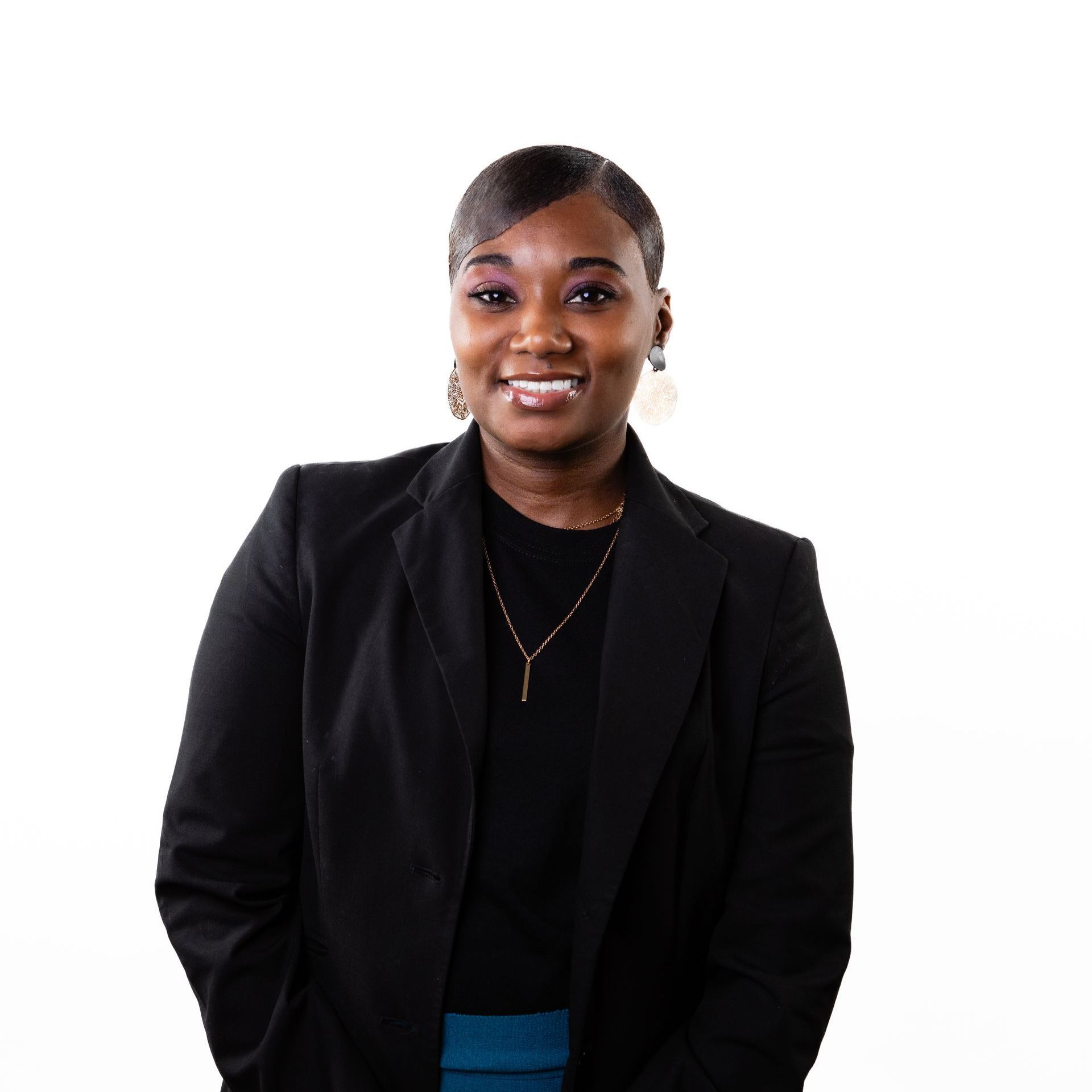 A woman wearing a black jacket and a necklace is smiling.