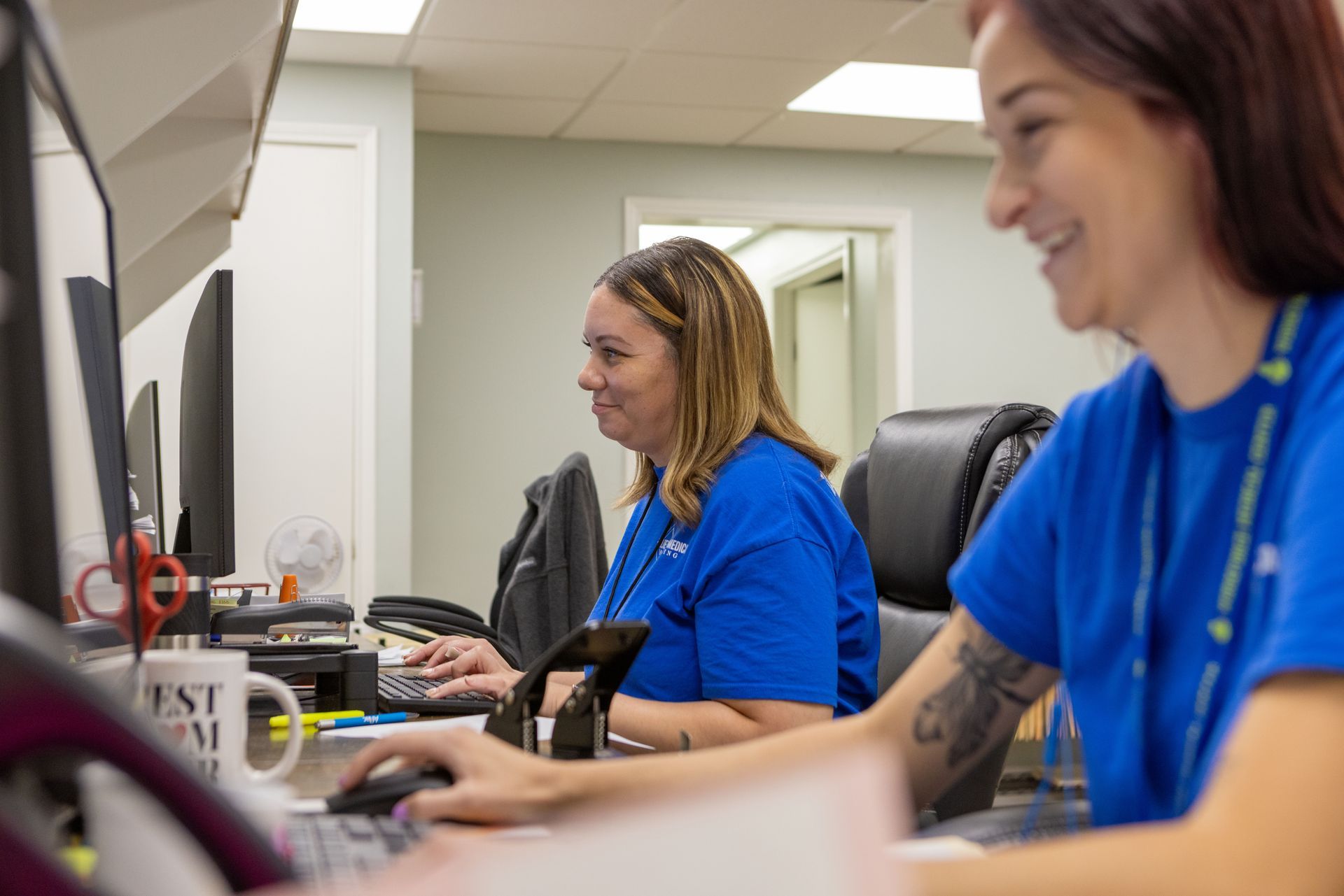 Two women are sitting at a desk in front of a computer.