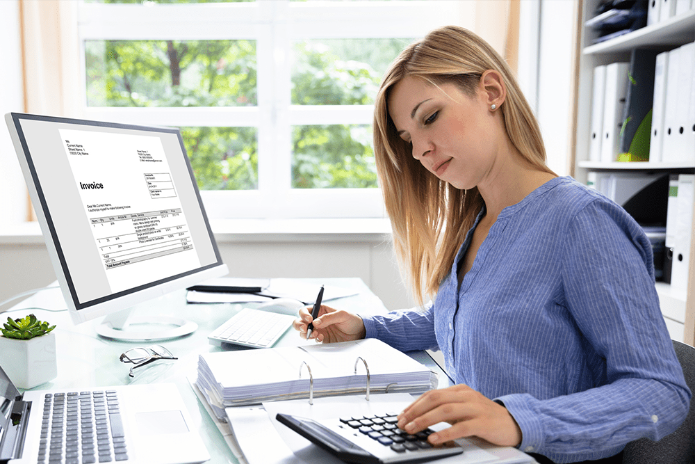 A woman is sitting at a desk with a computer and a calculator.