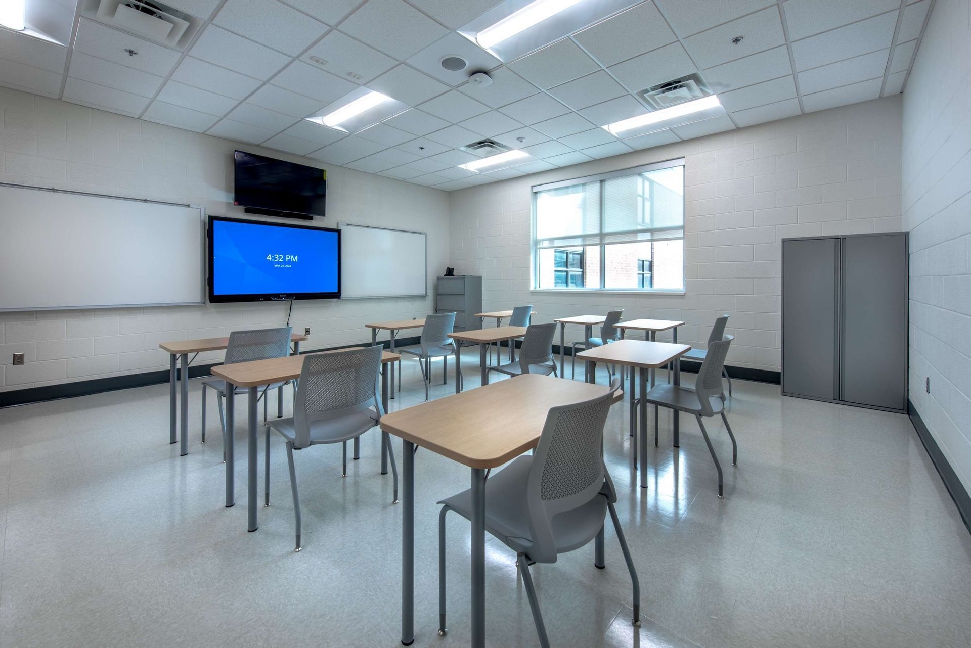 A classroom with tables and chairs and a flat screen tv on the wall.