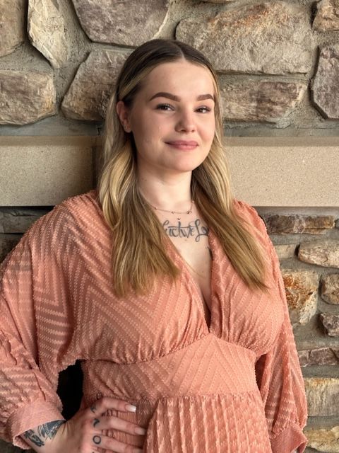 A woman in a pink dress is standing in front of a stone wall.