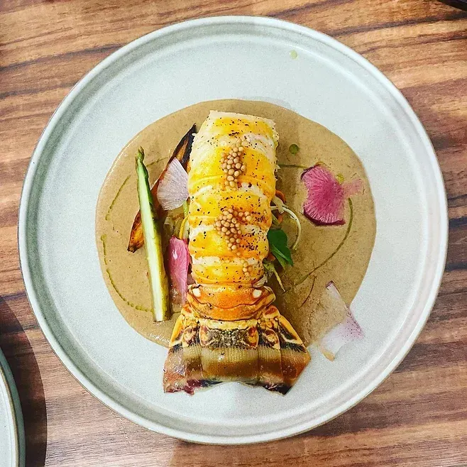 A white plate topped with a lobster tail on a wooden table.