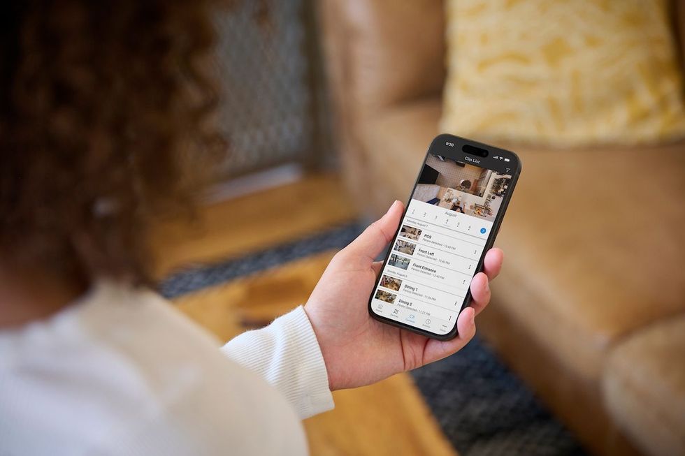 Hand holding a smartphone showing a home security camera app beside two dome cameras on a desk