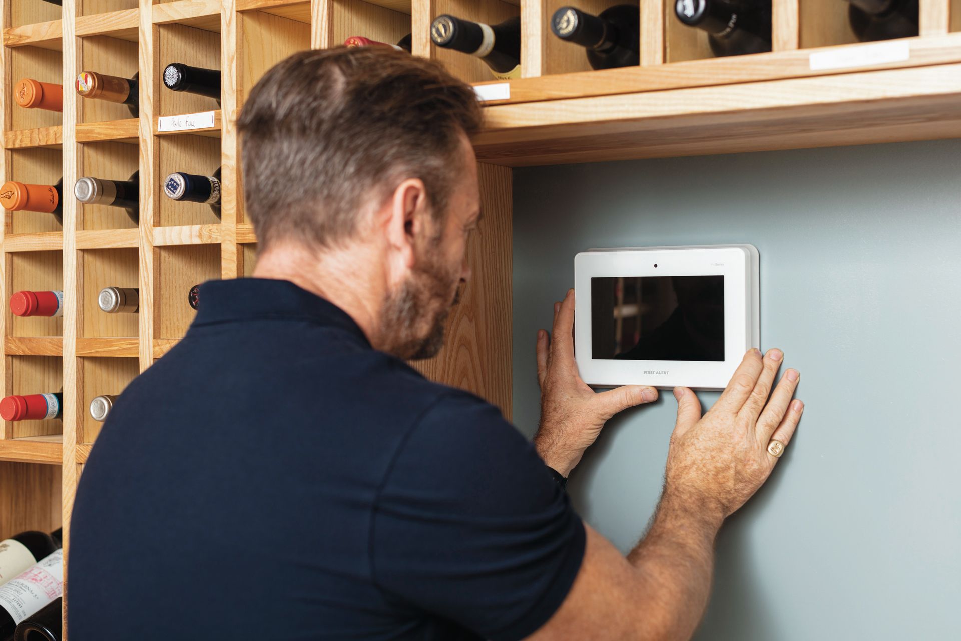 Technician mounting a white wall tablet controller beside a wine rack